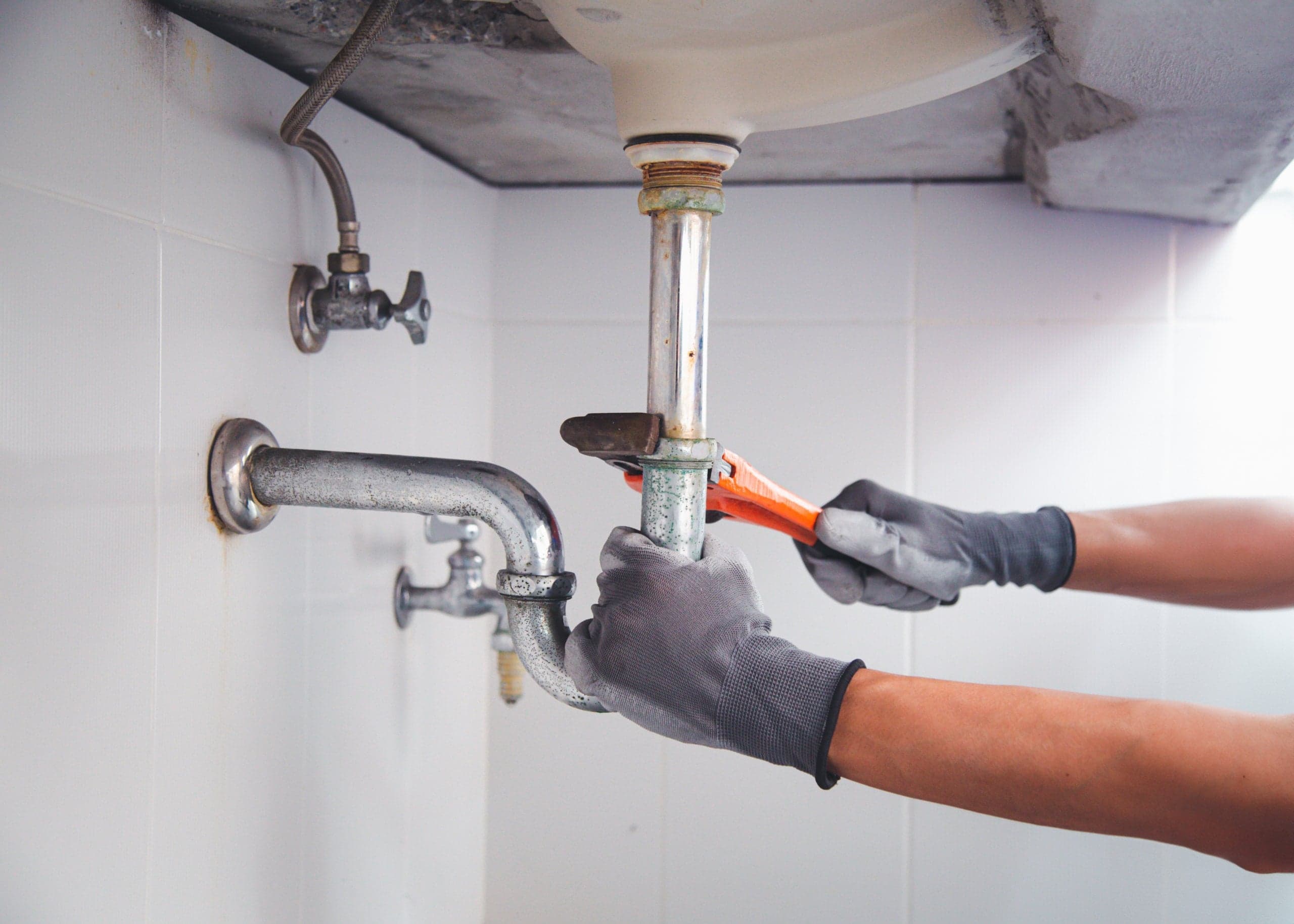 Plumber's gloved hands fitting a pipe beneath a sink